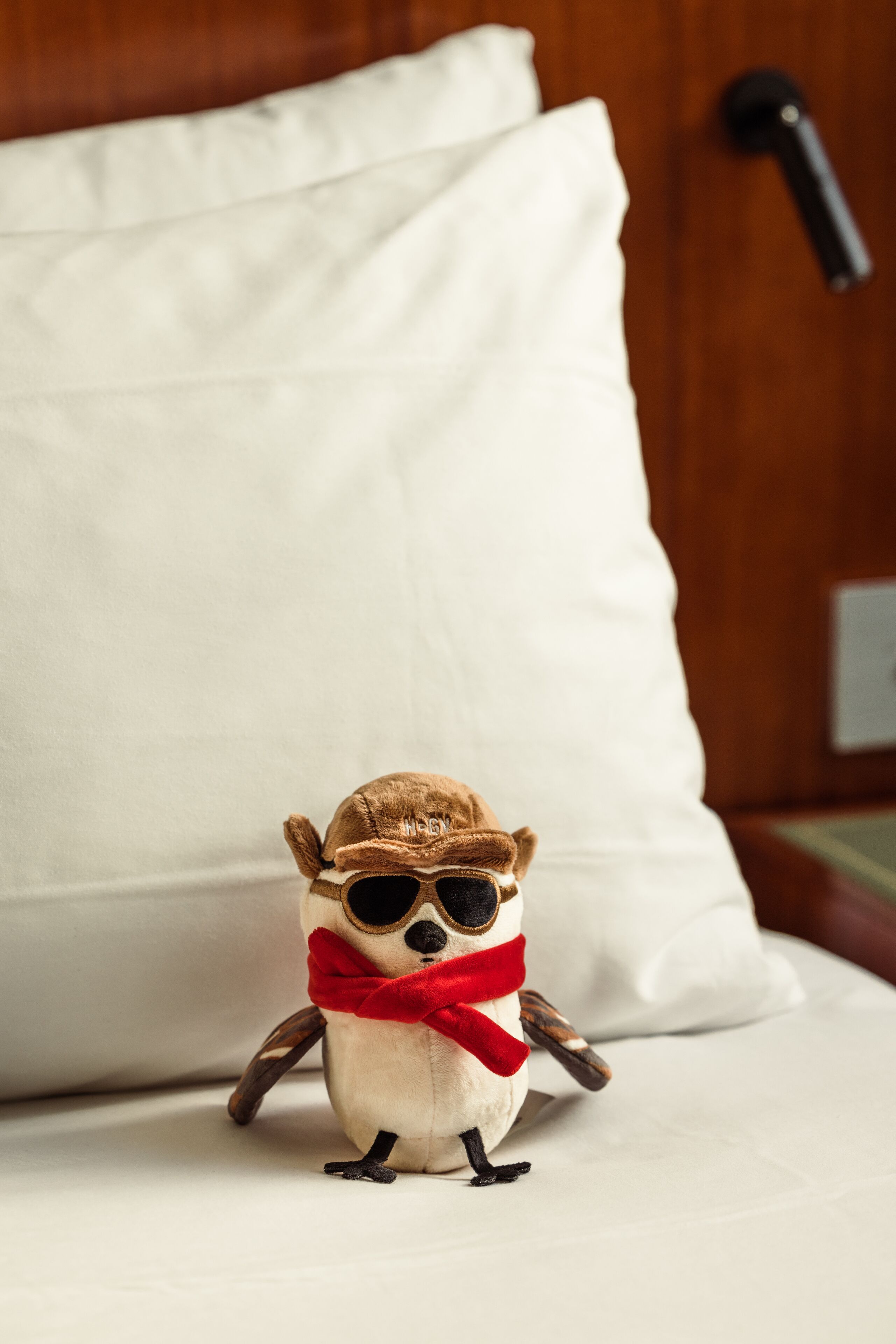 A plush toy on a bed with a white pillow and a wooden headboard.