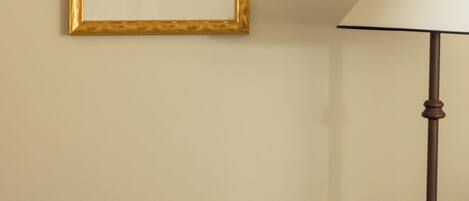 Una obra de arte enmarcada en una pared, una lámpara y una cama con cubrecolor blanco.