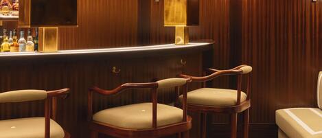 A bar area with wooden paneling, a bar counter, and three wooden bar stools.