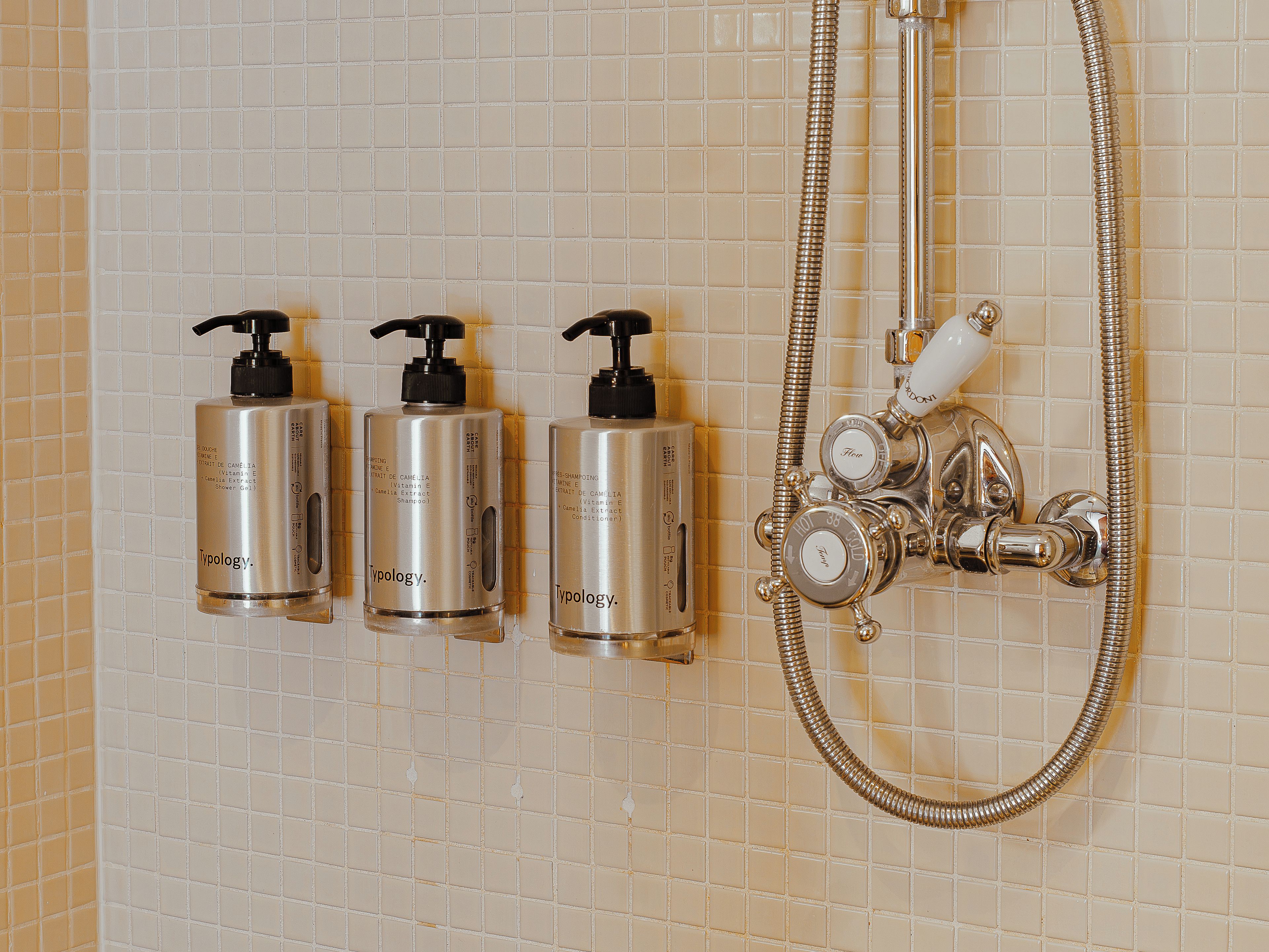 Baño con tres botellas de productos de la línea Typology y un cabezal de ducha cromado.