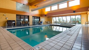 An indoor swimming pool with clear water, tiled floors, and sunlit windows.