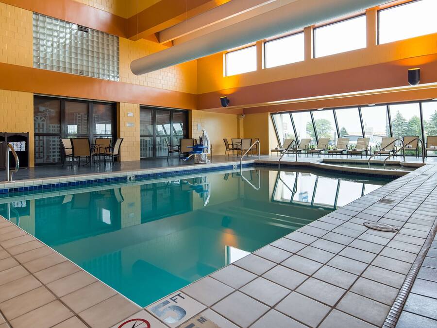 An indoor swimming pool with clear water, tiled floors, and sunlit windows.