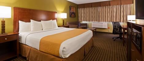 Quarto de hotel com uma cama grande, uma escrivaninha, uma cadeira, uma televisão e um aparelho de ar condicionado.