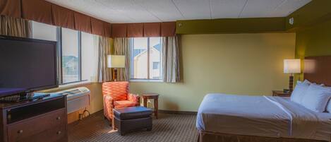 A hotel room with a bed, a TV, a chair, a desk, and a window.