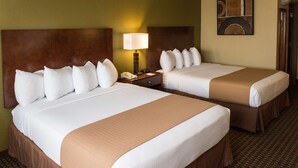 A hotel room with two beds, each with white linens and brown headboards. There is a nightstand with a lamp and a telephone between the beds.