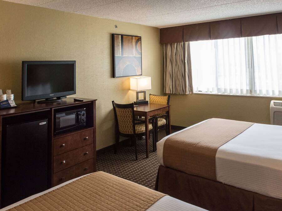 A hotel room with two beds, a desk with a TV, a microwave, and a chair.