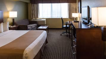 Une chambre d’hôtel avec un grand lit, un bureau avec un ordinateur, une chaise, un canapé, une télévision et une fenêtre avec des rideaux.