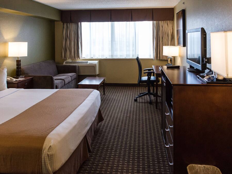 Une chambre d’hôtel avec un grand lit, un bureau avec un ordinateur, une chaise, un canapé, une télévision et une fenêtre avec des rideaux.