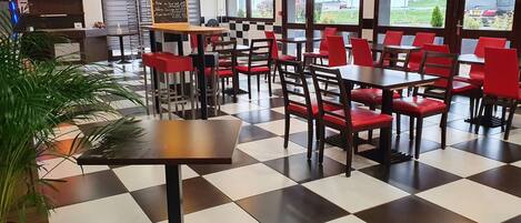 A restaurant interior with a checkered floor, red and black chairs, and pendant lighting.
