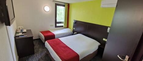 Une chambre d’hôtel avec deux lits, un bureau, une fenêtre avec des rideaux et un climatiseur fixé au mur.