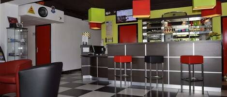 Zona de bar con piso a cuadros, taburetes de bar negros y rojos, y una barra con varias botellas.