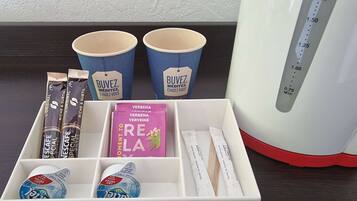 A white tray with various items including two blue paper cups, a white coffee maker, and a box containing a pink box labeled "VERBENA VERBEINE," a blue yogurt container, and several other items.
