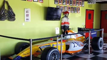 A racing car on display with a checkered floor, a mannequin in racing gear, and a wall of racing posters.