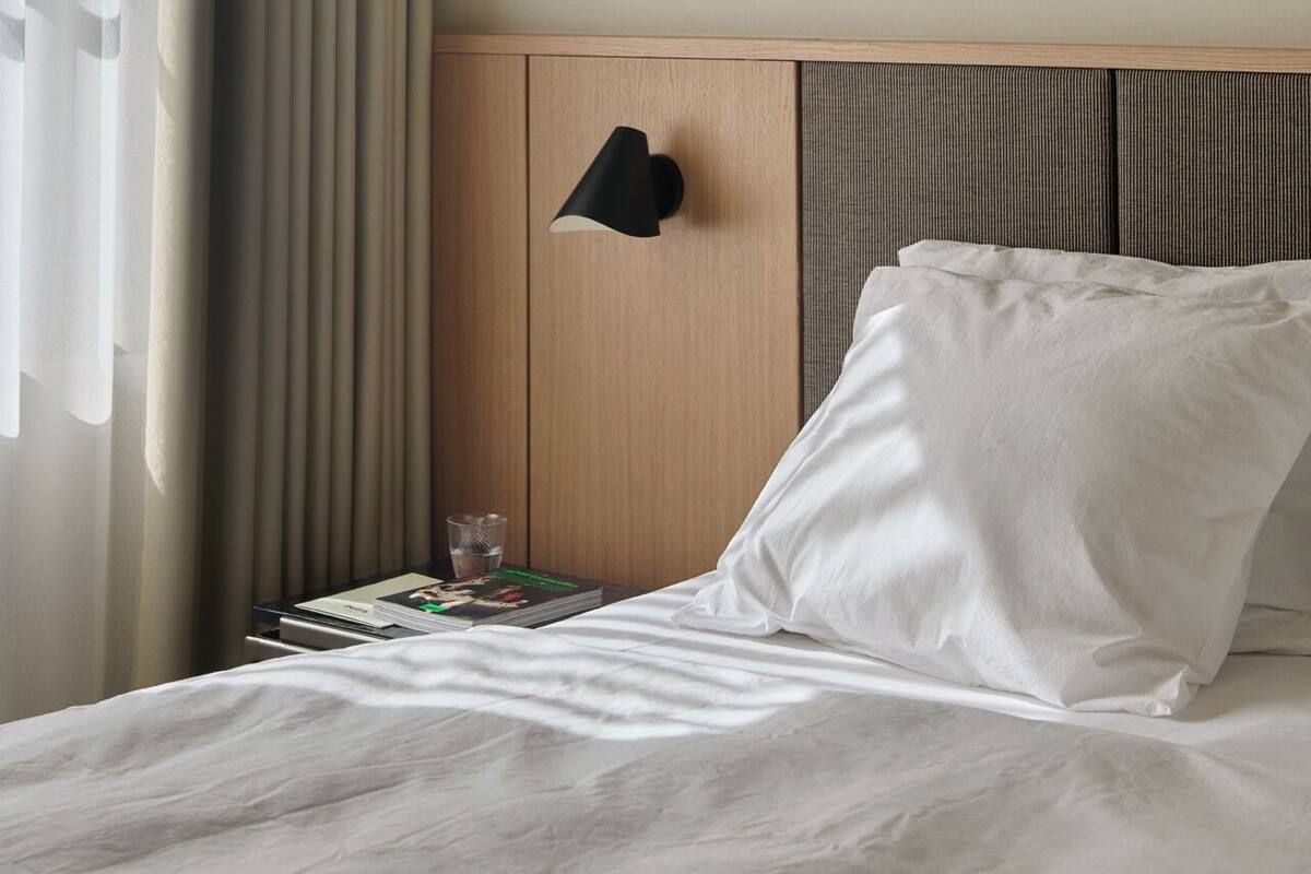 A hotel room with a bed, a nightstand, a lamp, and a window with curtains.