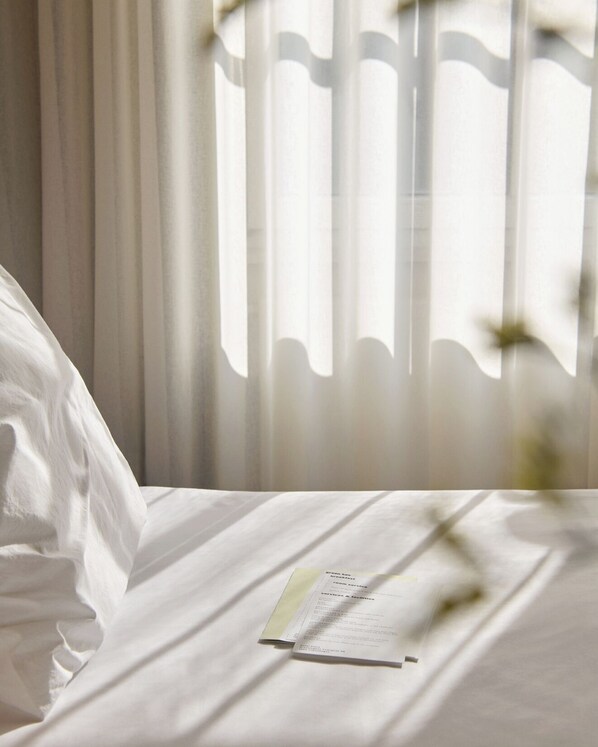 A neatly made bed with a menu on it, curtains in the background, and a window with light coming through.