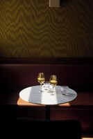 Mesa redonda con tres copas de vino y un cuenco pequeño, frente a una pared con diseño.