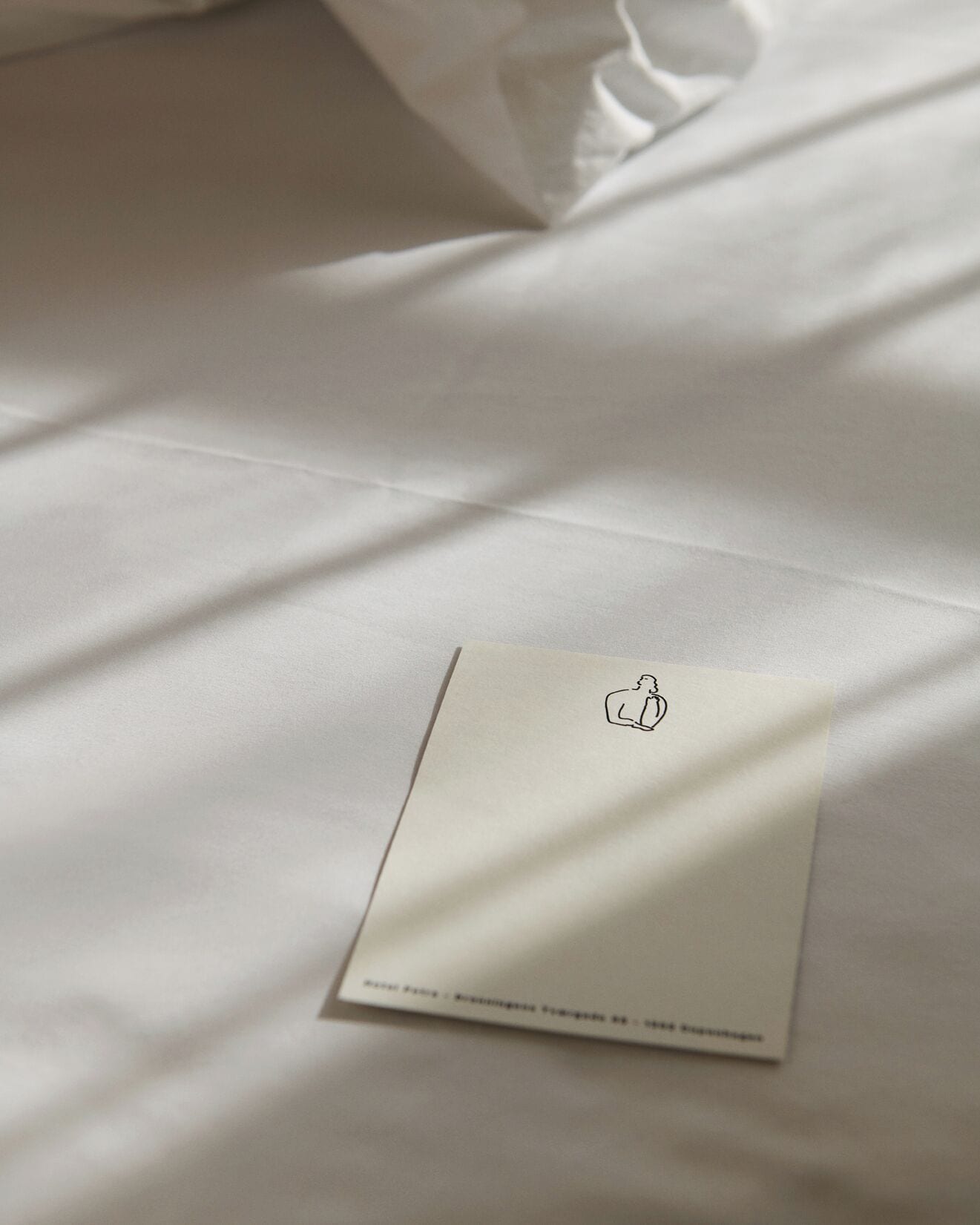 Una cama bien hecha con sábanas blancas y una pequeña tarjeta con un logotipo y texto.
