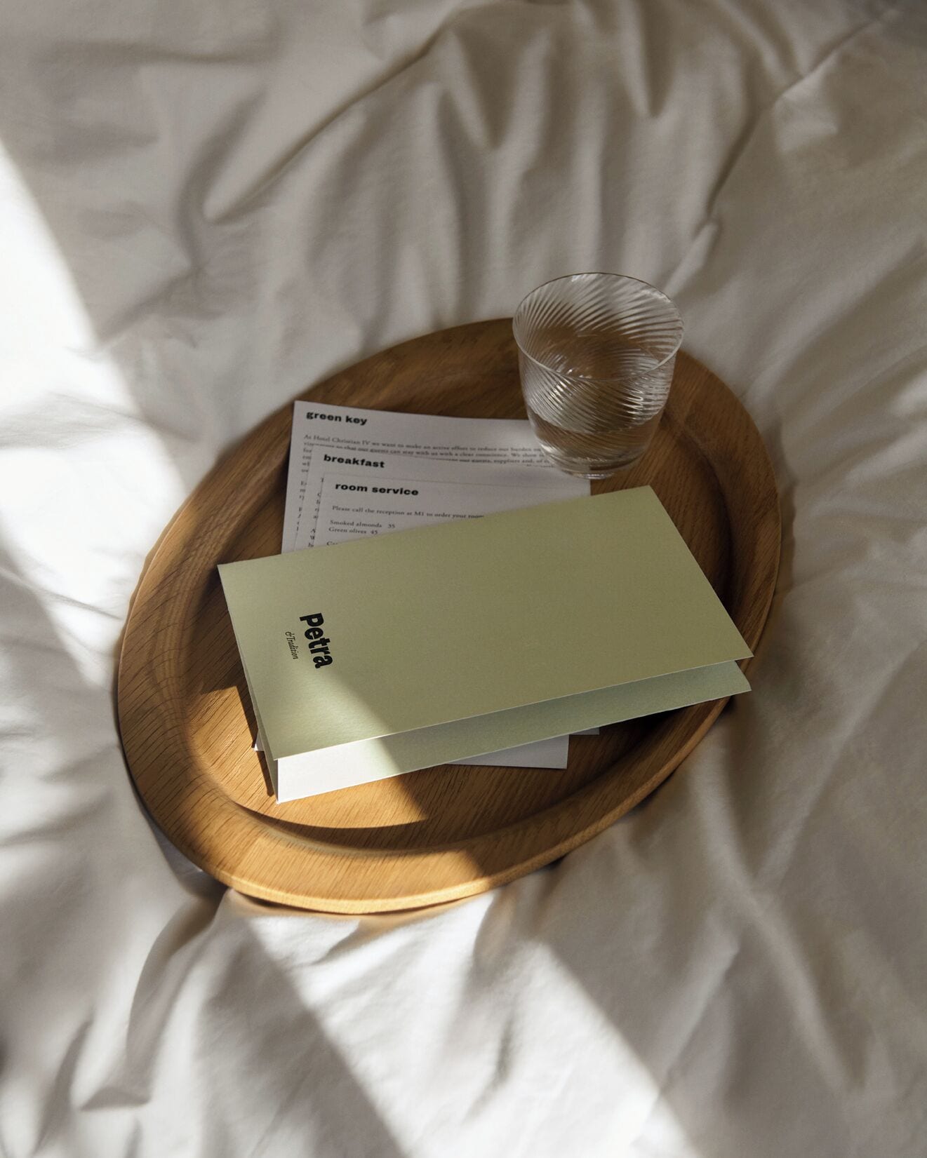 Un vassoio di legno con un bicchiere d'acqua, un menu e un libro su un letto.