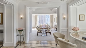 A spacious hotel lobby with a grand chandelier, a dining area with a long table, and a reception desk.