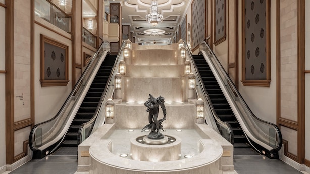 A grand lobby with two escalators, a central fountain, and ornate wall panels.