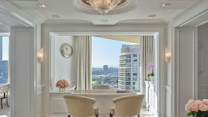 A spacious room with a large window offering a city view, a chandelier, and two chairs facing a table. - The Langham, Melbourne (Southbank)