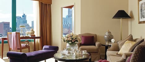 Ein Hotelzimmer mit Blick auf die Stadt, inklusive Sofa, Sessel, Tisch mit Blumenvase und Lampe.