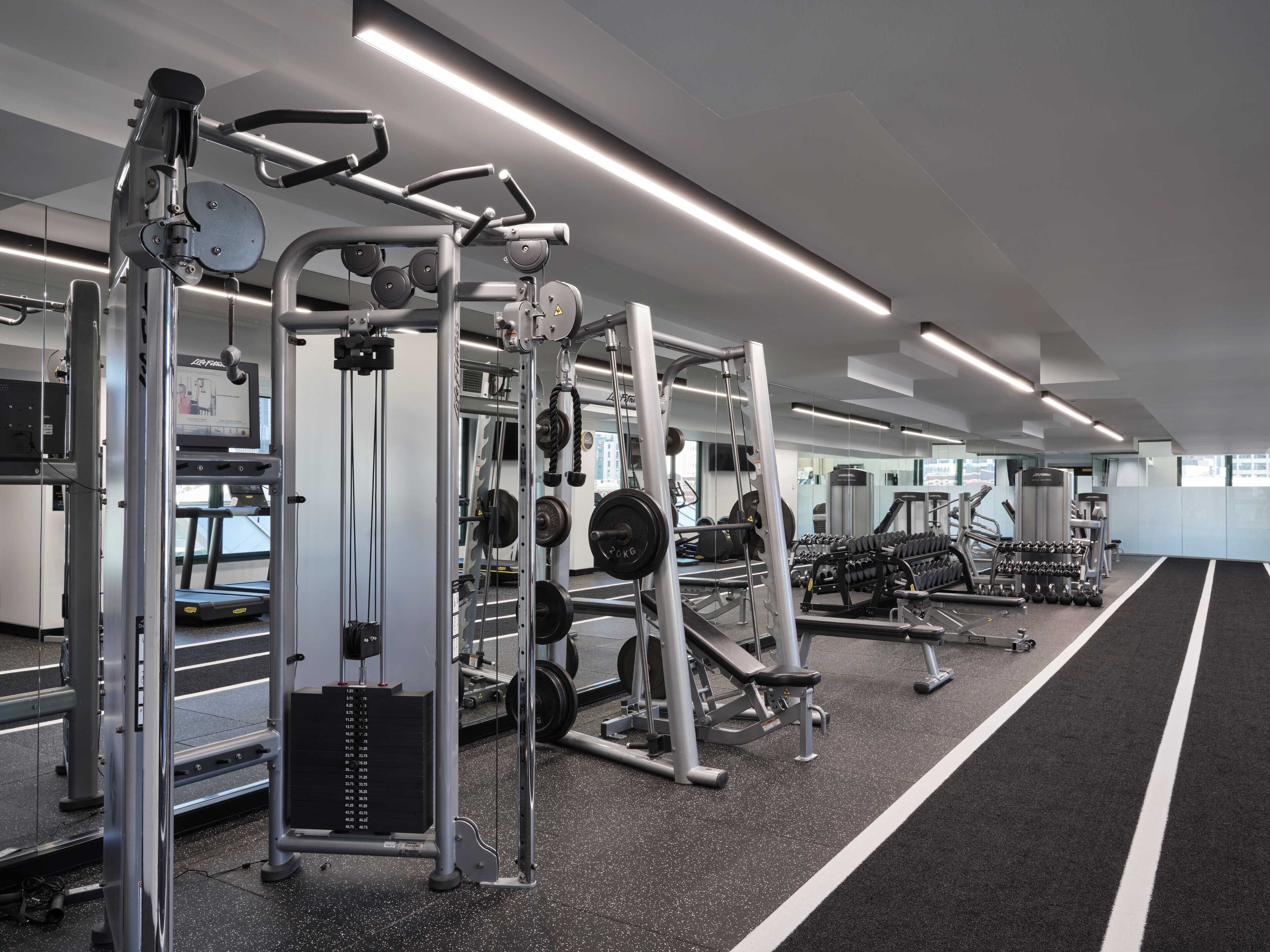 Un gimnasio moderno con equipo de levantamiento de pesas, cintas de correr y un espejo grande.