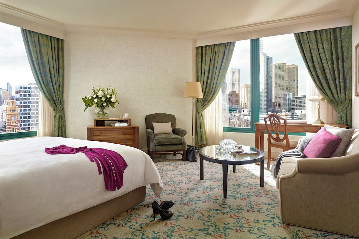 A hotel room with a bed, a chair, a table, and a sofa.