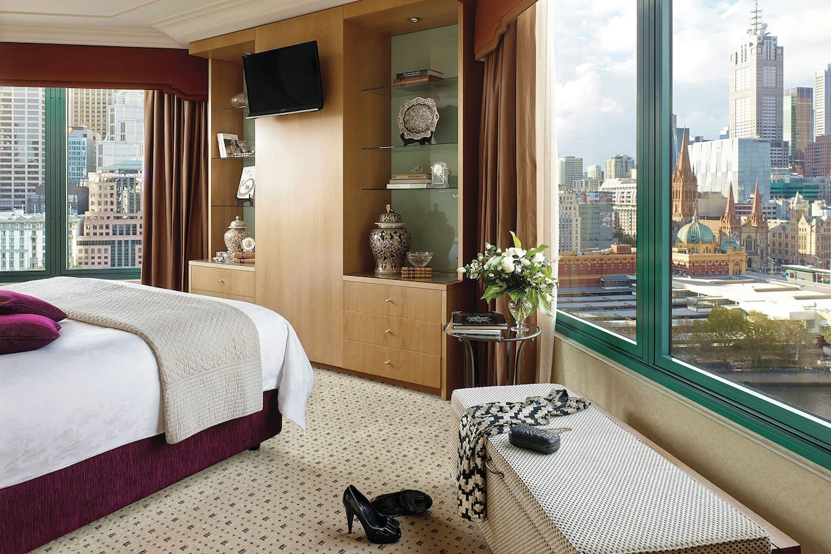 A hotel room with a large window, a bed, a vanity with a mirror, and a view of the cityscape.