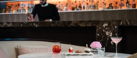 Una zona de bar con una mesa de mármol, una copa de martini, un plato de postre y una copa de cóctel.
