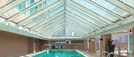 A swimming pool with a glass ceiling, surrounded by walls and a clock.