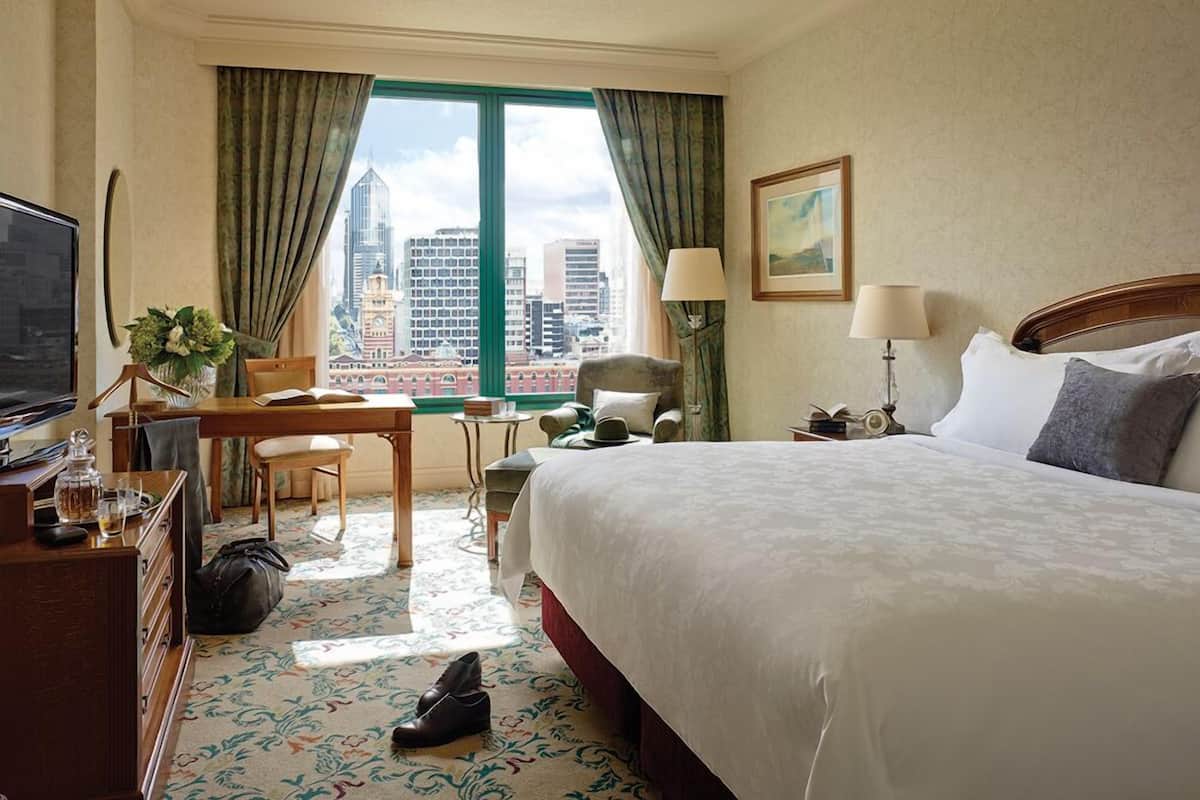 A hotel room with a large bed, a desk, a chair, a television, and a view of the cityscape.