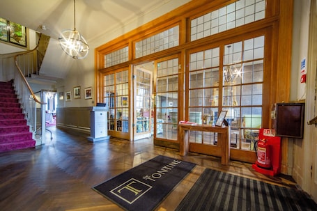 A hotel lobby with a grand staircase, a reception desk, and a fire extinguisher.