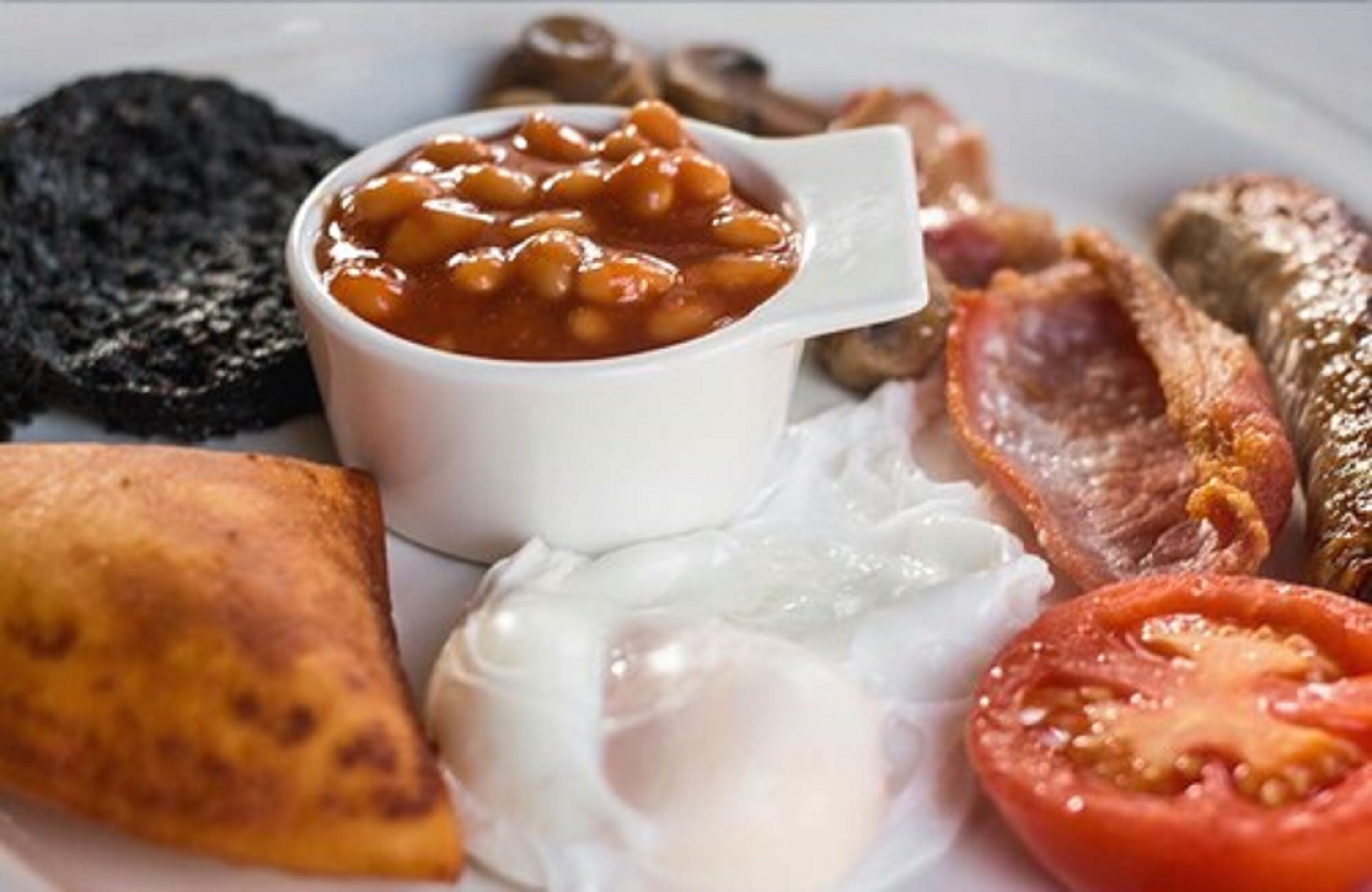 A plate of breakfast food including beans, bacon, eggs, and a slice of tomato.