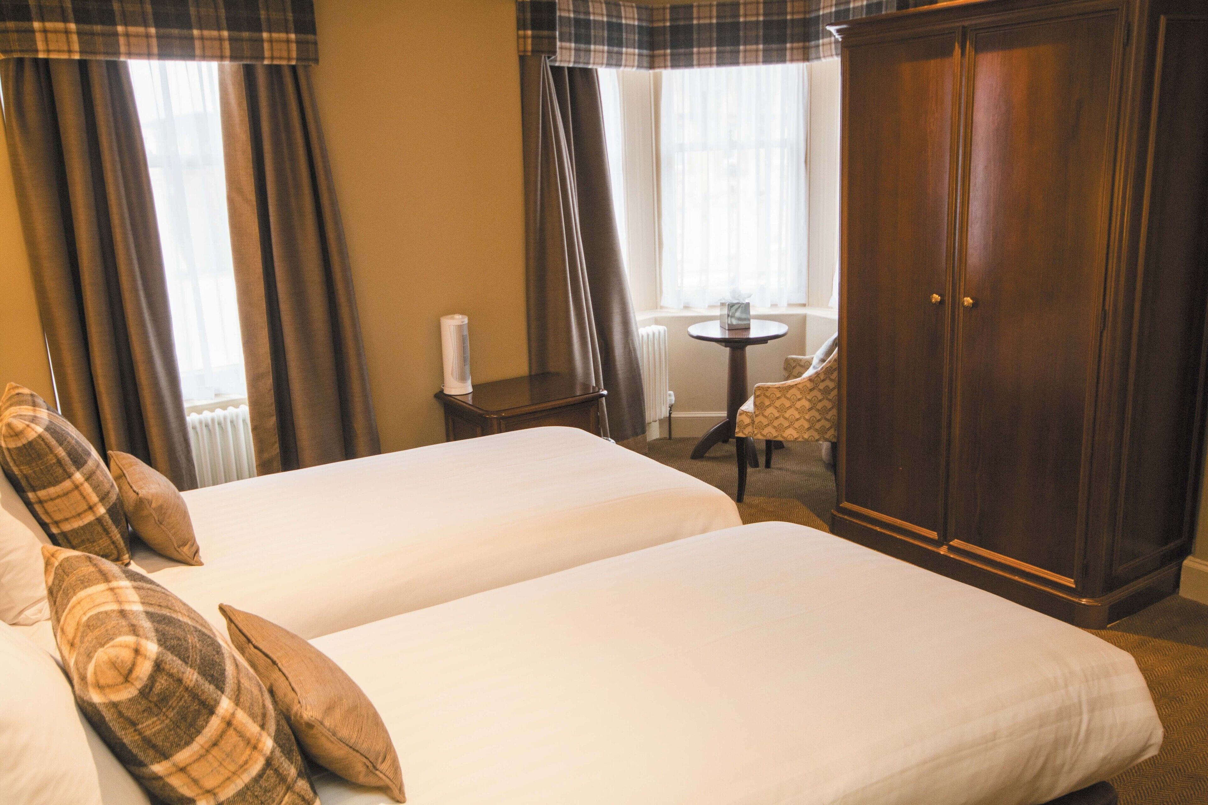 Habitación de hotel con dos camas, un armario, una mesita y una silla.