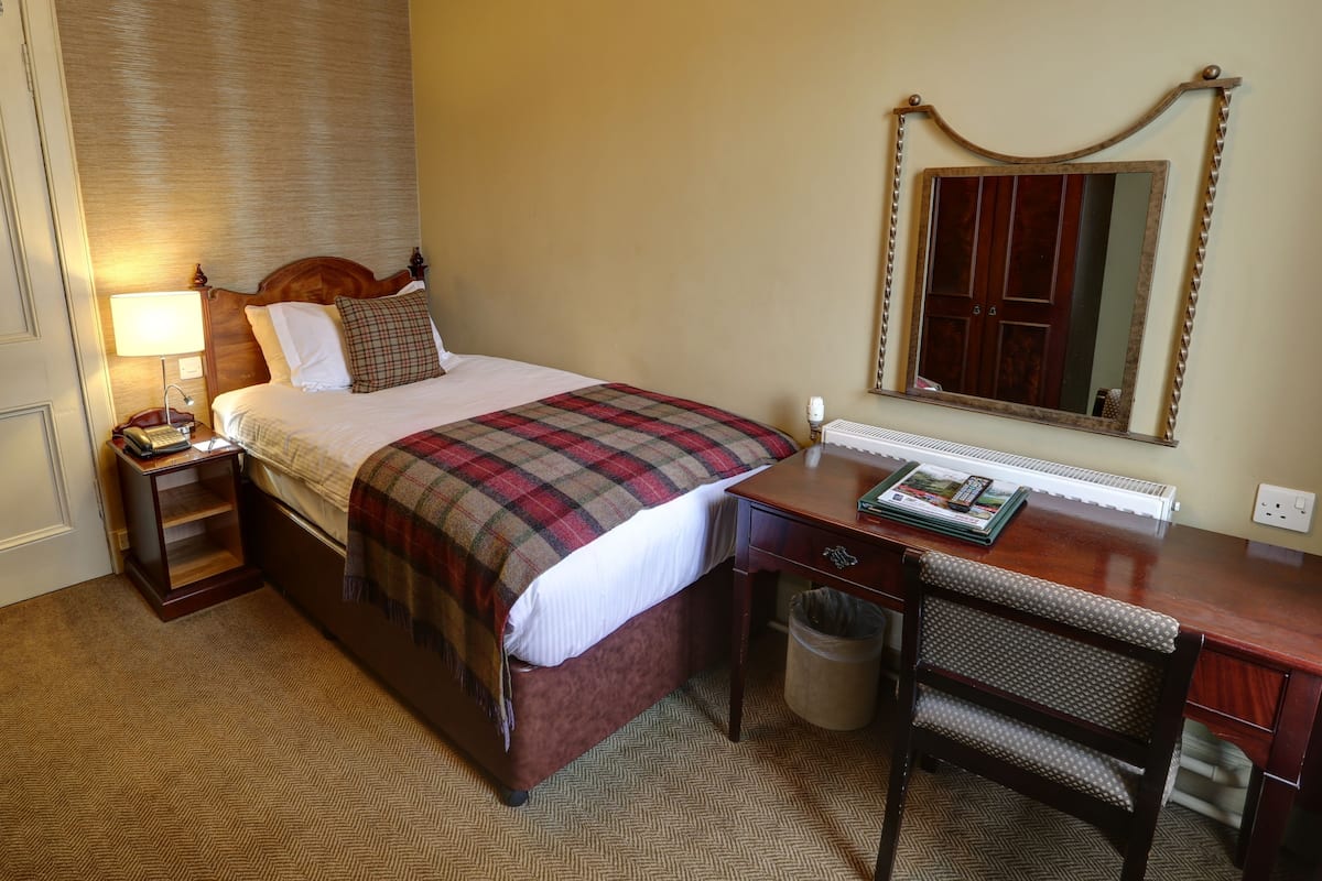 A hotel room with a bed, bedside table, lamp, desk, chair, and a mirror.