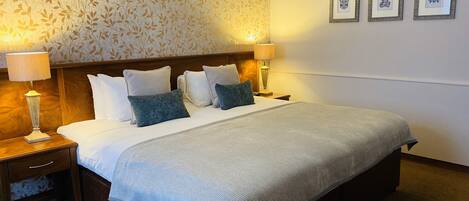 A hotel room with a large bed, two bedside tables, a nightstand, a patterned wallpaper, and three framed pictures on the wall.