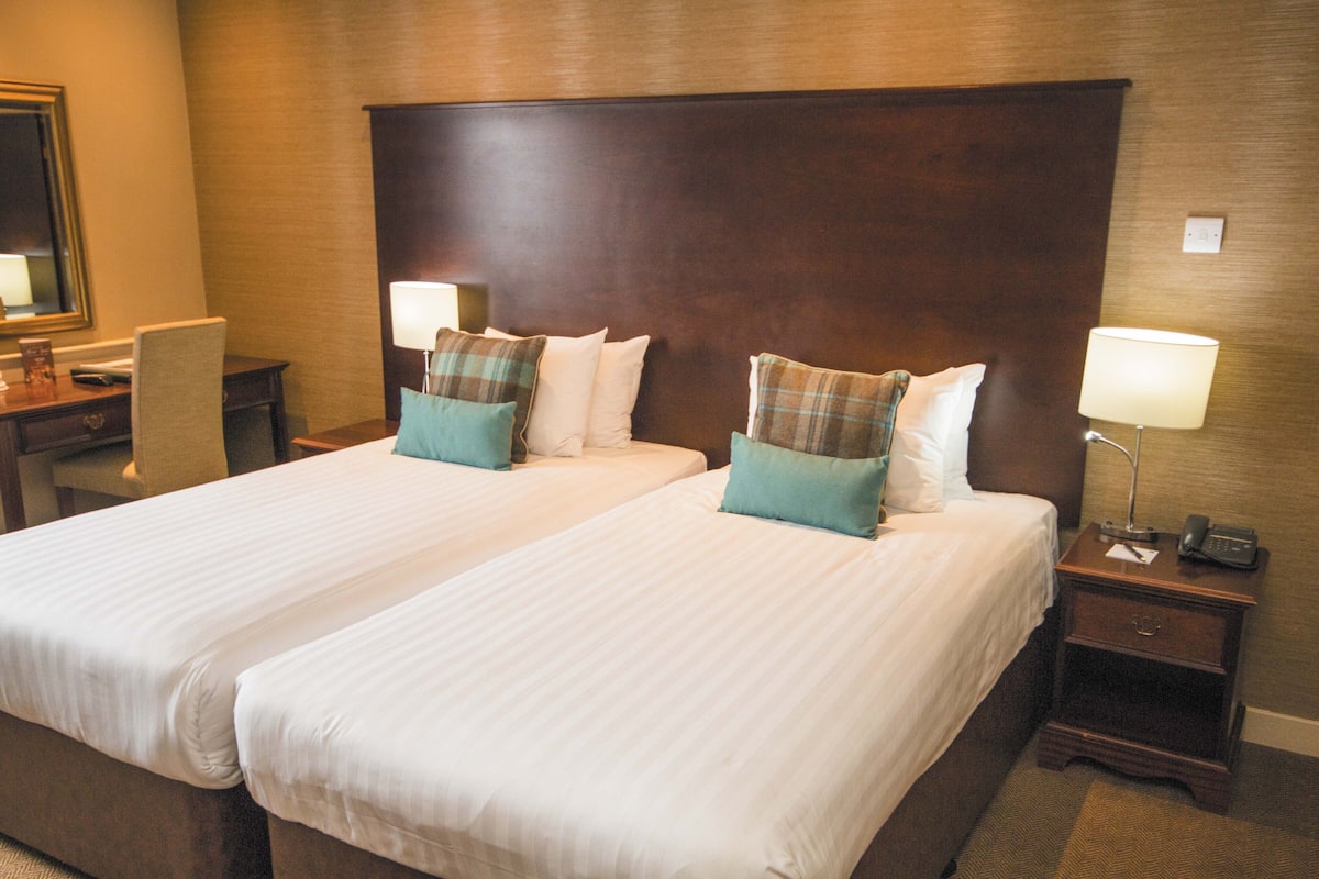 A hotel room with two beds, a wooden headboard, bedside tables with lamps, and a mirror on the wall.