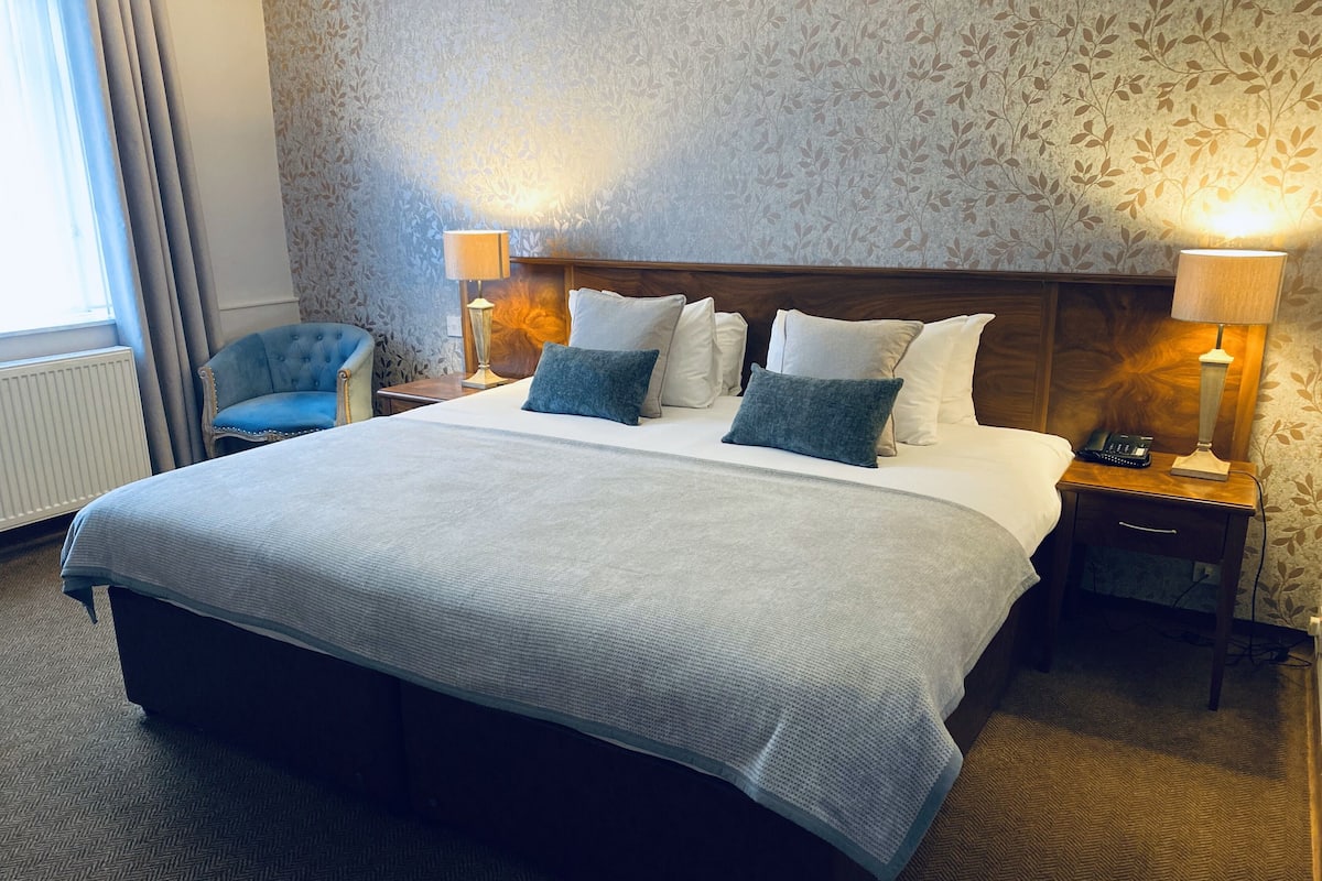 A hotel room with a large bed, two bedside tables with lamps, a chair, and a radiator.