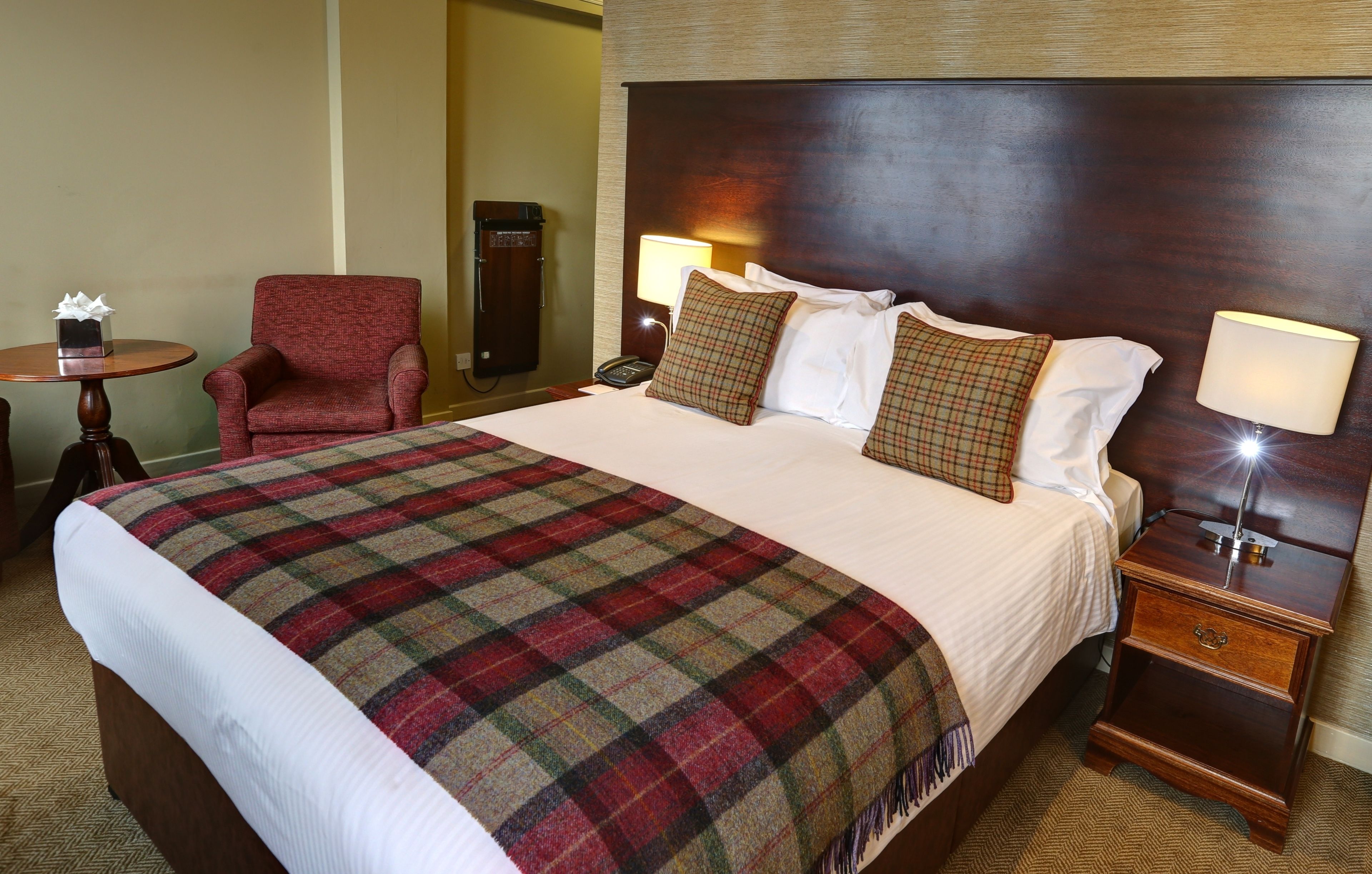 A hotel room with a large bed, a red armchair, a bedside table with a lamp, and a telephone.