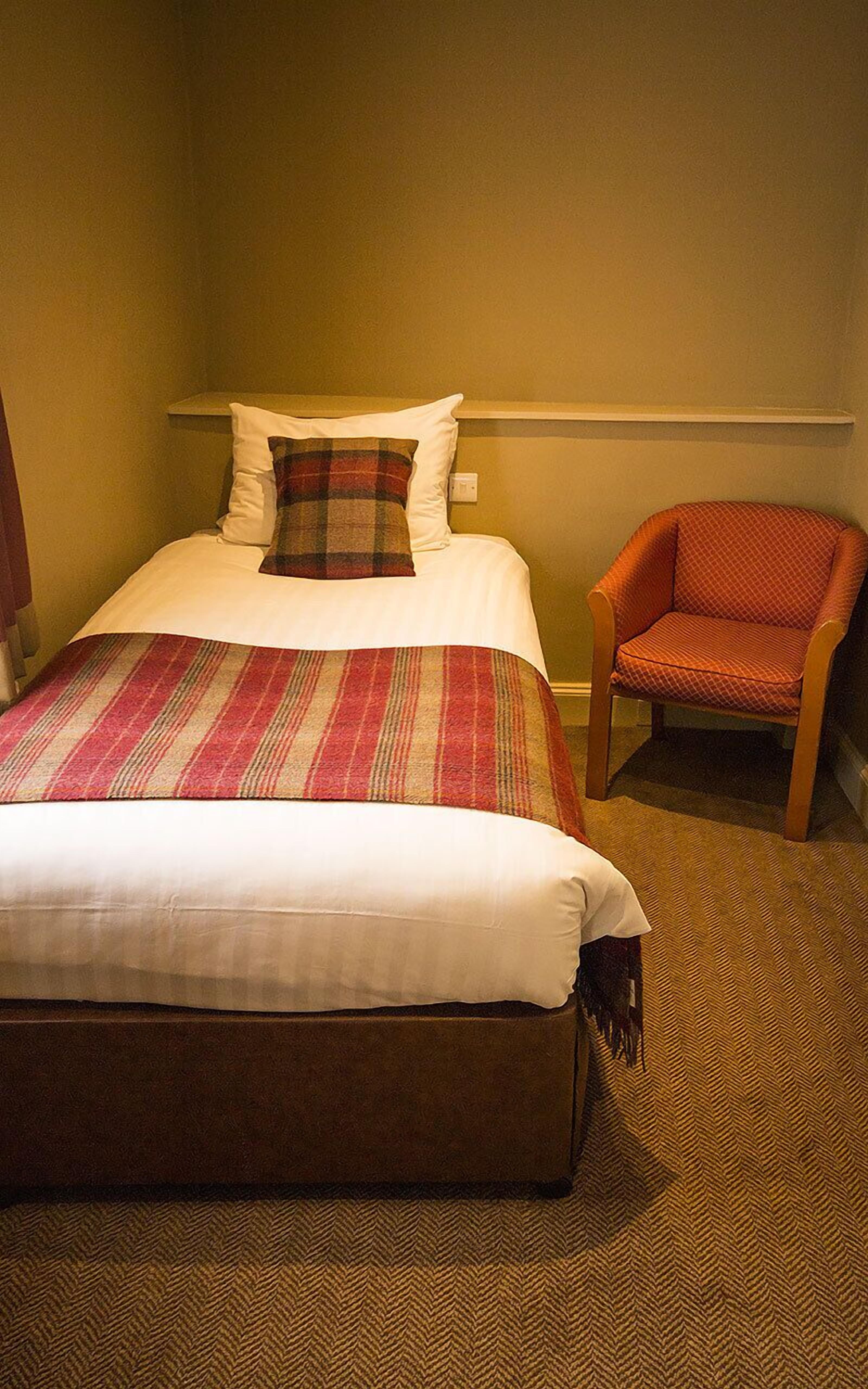 A hotel room with a bed, a chair, and a carpeted floor.