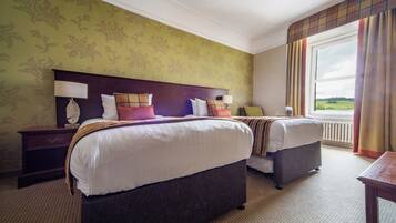 A hotel room with two beds, a nightstand, a lamp, and a view of the outdoors.