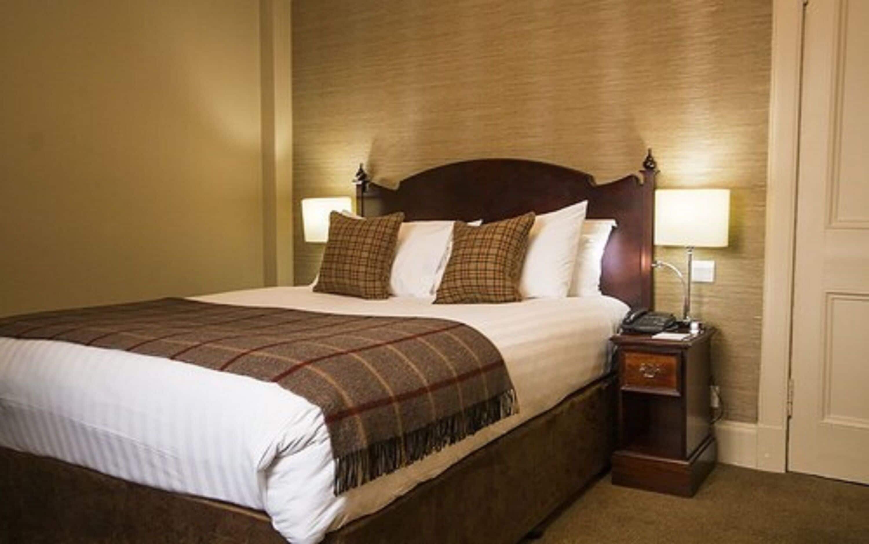 A hotel room with a large bed, two bedside lamps, a nightstand, and a door.