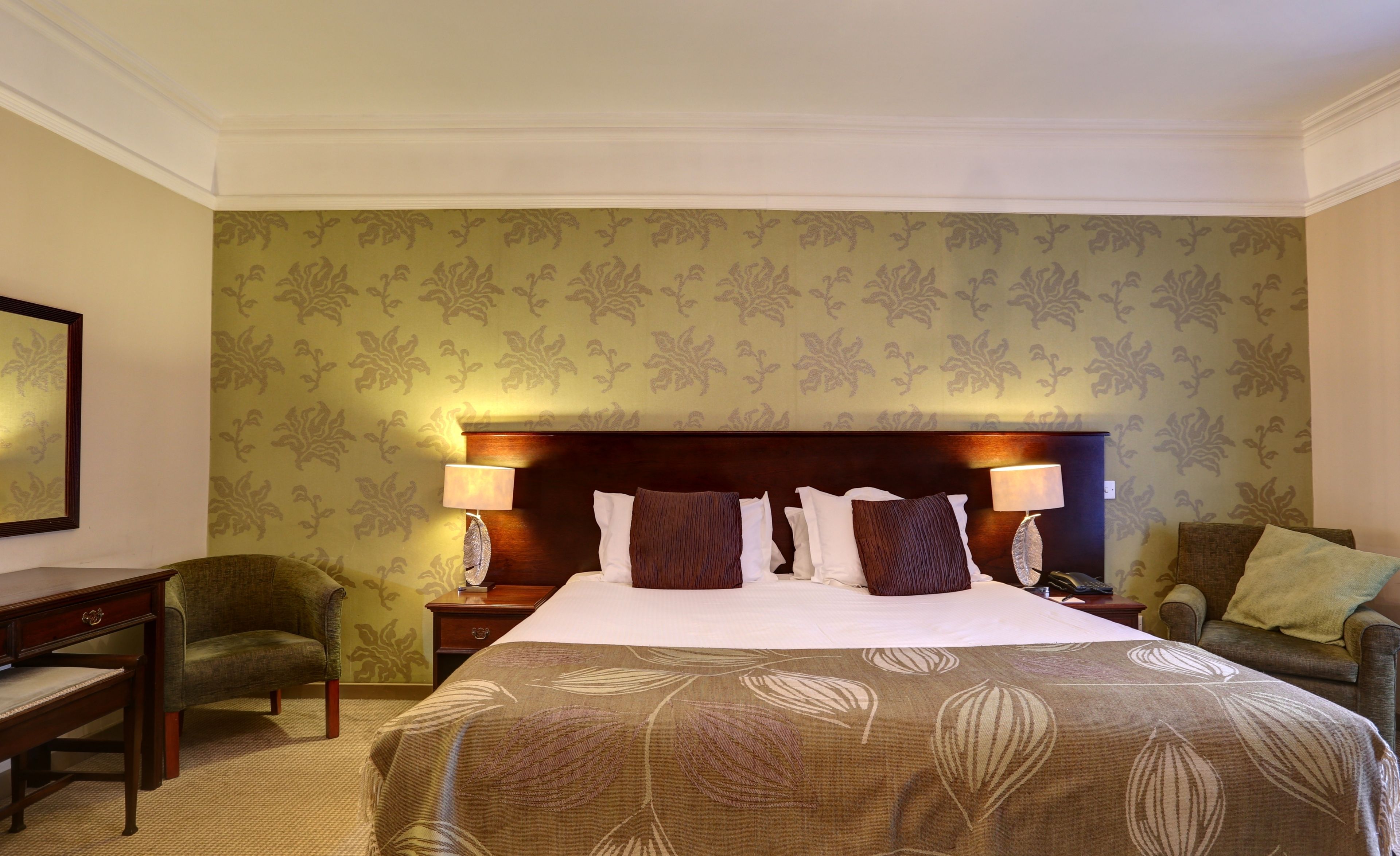 A hotel room with a large bed, two bedside lamps, a nightstand, a desk, and two armchairs.