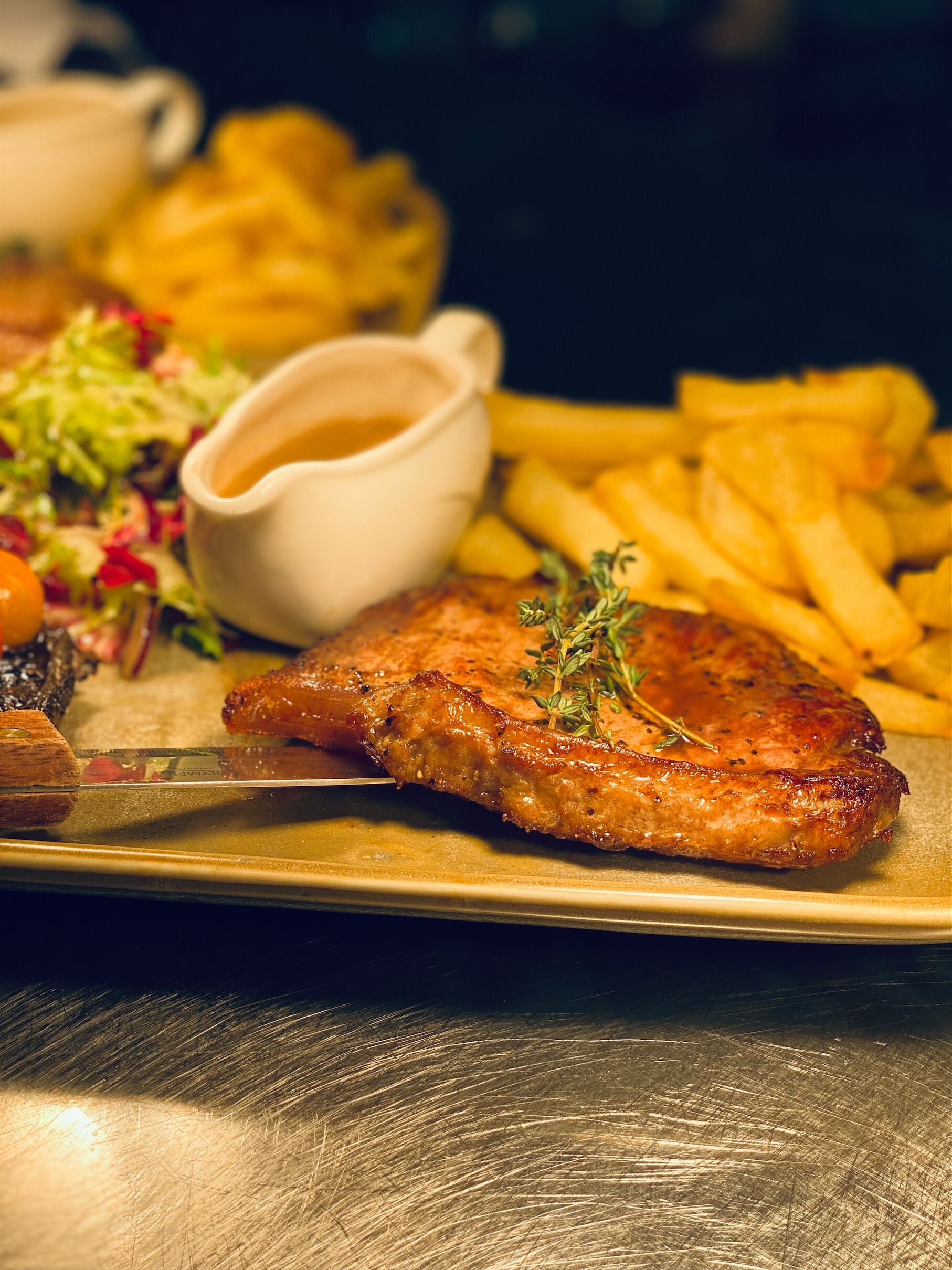 A plate with a grilled steak, French fries, a salad, and a small bowl of sauce.