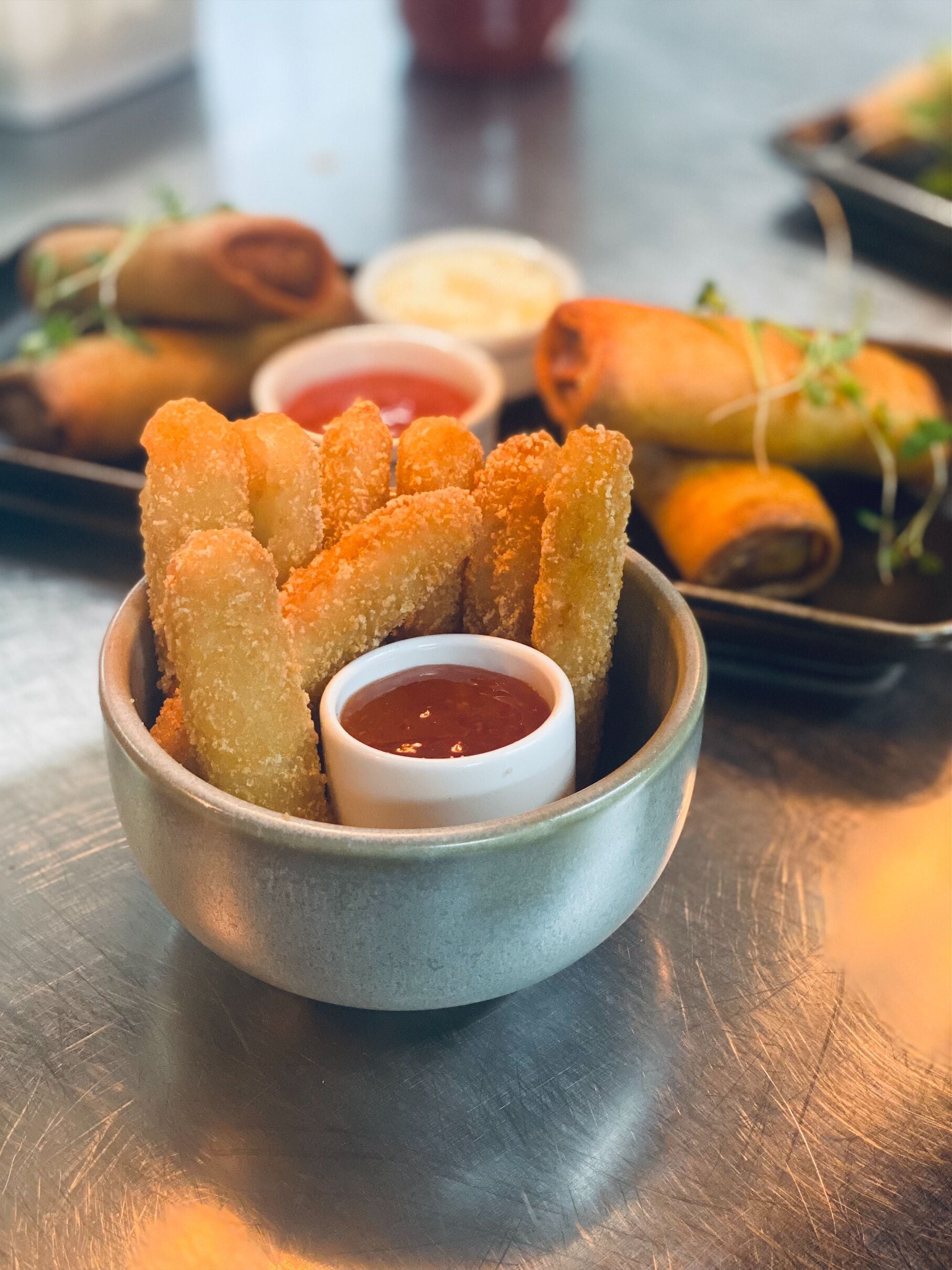 A bowl of breaded and fried food items, possibly spring rolls, accompanied by a small bowl of dipping sauce.