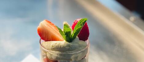 A dessert in a clear glass with strawberries, banana slices, and whipped cream, served on a metal tray with a spoon and napkin.