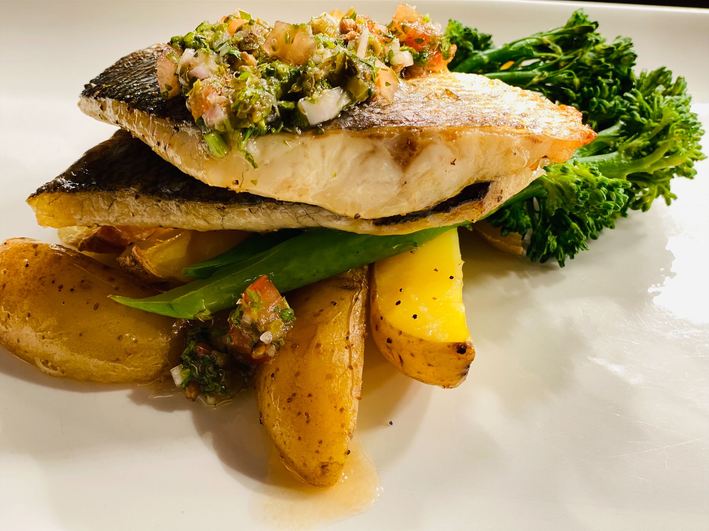 A plate with a piece of fish, roasted potatoes, and a green vegetable.