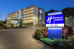 Un hotel Holiday Inn Express con diseño moderno, que presenta un gran letrero y jardines bien cuidados.