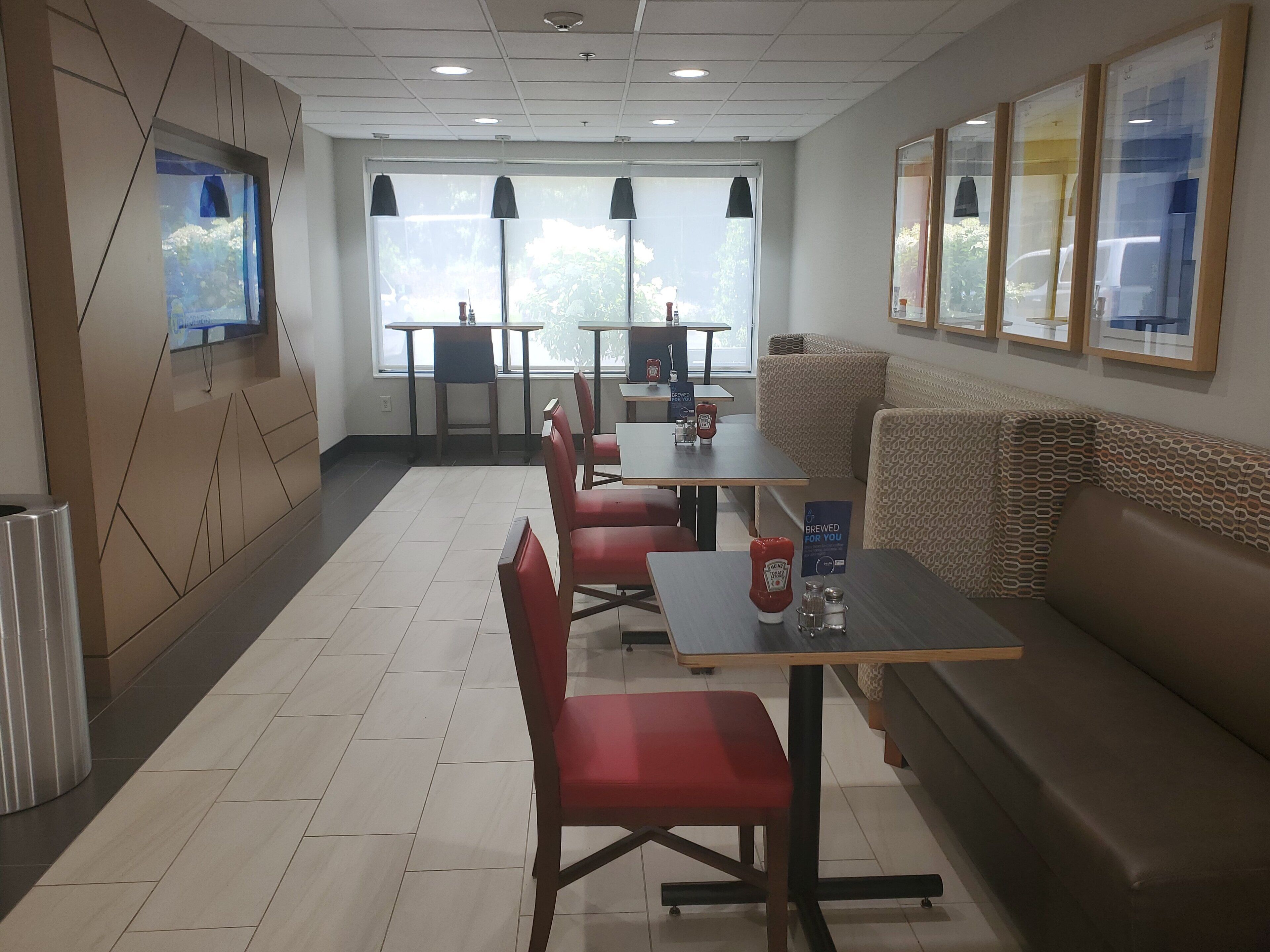 A modern restaurant with a long counter, red chairs, and a sofa. There are tables with condiments and a sign indicating the beer is brewed for you.